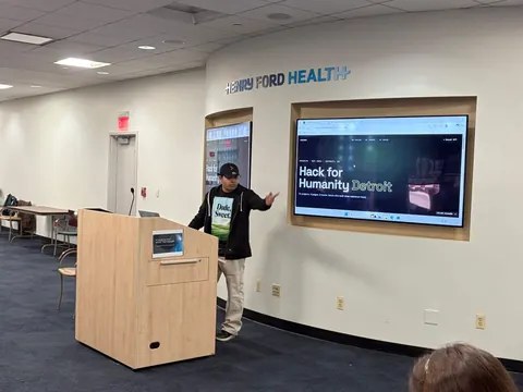 Judge Rishiraj Sarkar gesturing toward the Hack for Humanity Detroit results page on the big screen