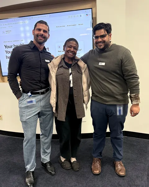 Three people smile in front of a screen showing the SisterCare Detroit website