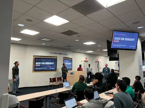 From left, Zlatan Cizmic, Saeb A. Ahsan, Donovan Brown, Siranjeev Venkateswaran and Josh Crites at the front of the room beside the Hack for Humanity Detroit slides as builders look on