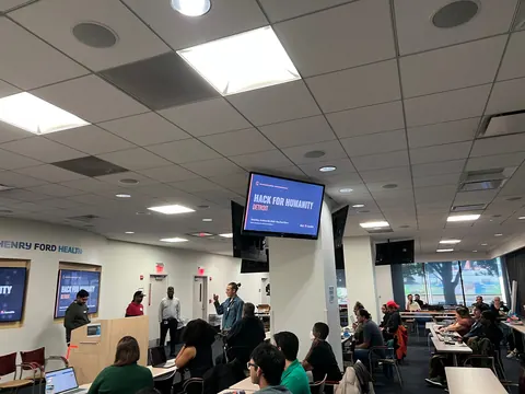 Builders seated at tables face Saeb A. Ahsan, Donovan Brown, Siranjeev Venkateswaran and Josh Crites at the front of the room, with the Hack for Humanity Detroit slide overhead